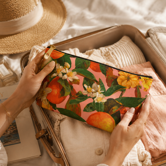 Person holding a floral orange blossom clutch with a suitcase and hat in the background