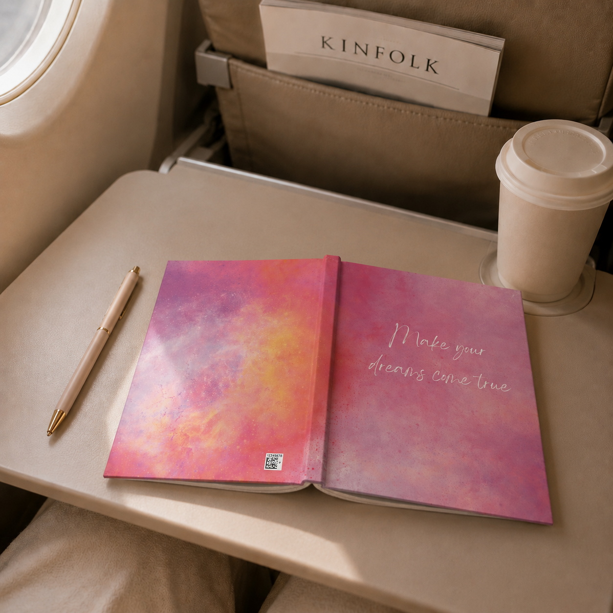 Open notebook with a motivational quote on an airplane tray table next to a pen and coffee cup.