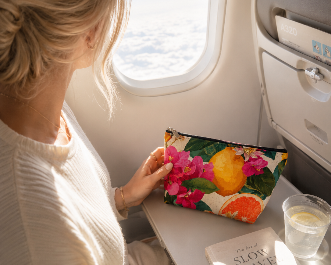 Woman on an airplane holding a floral pouch with a view of the sky through the window.