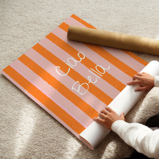 Person unrolling a pink and orange striped poster with 'Ciao Bella' text on a beige carpet.