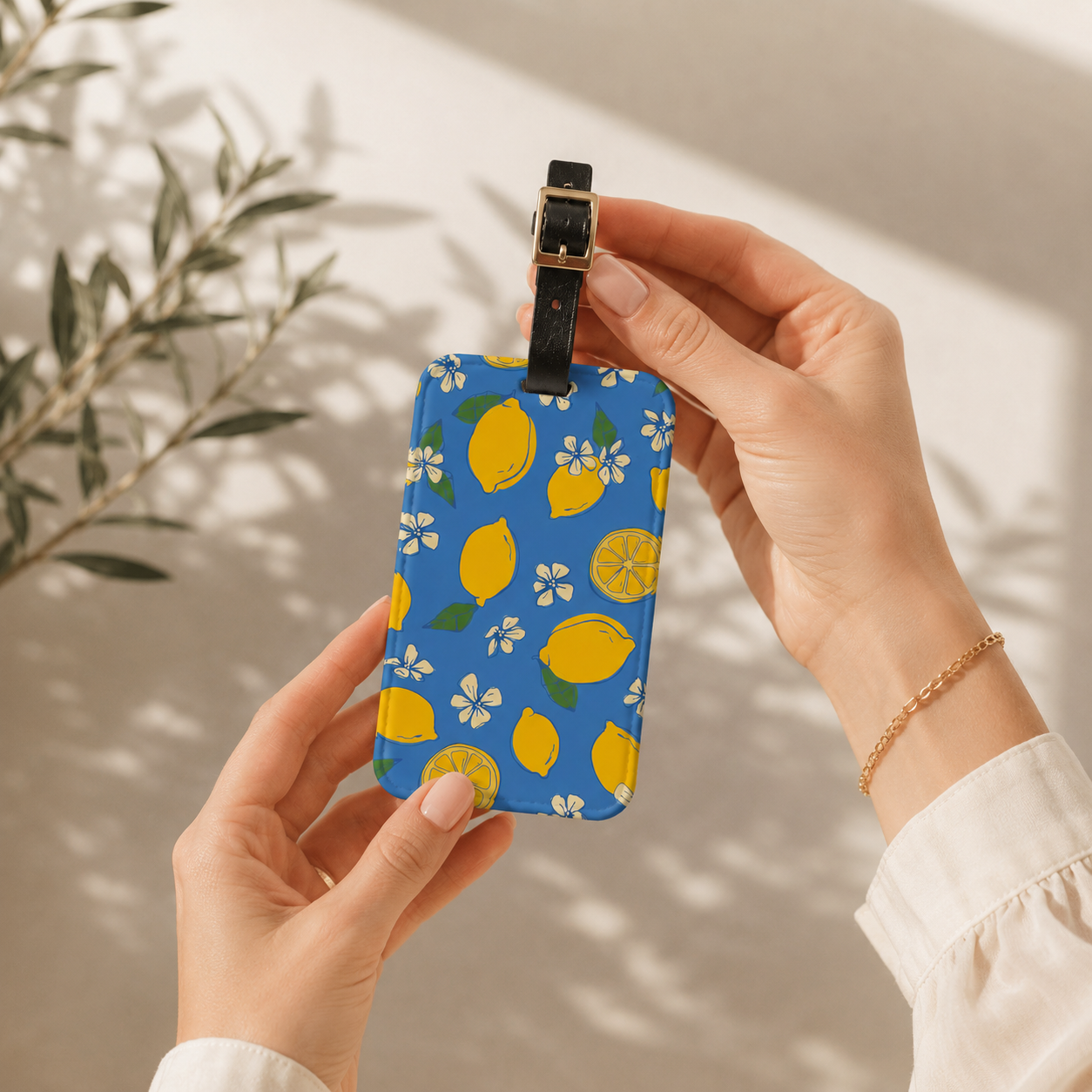 Hand holding a blue luggage tag with lemon pattern against a neutral background