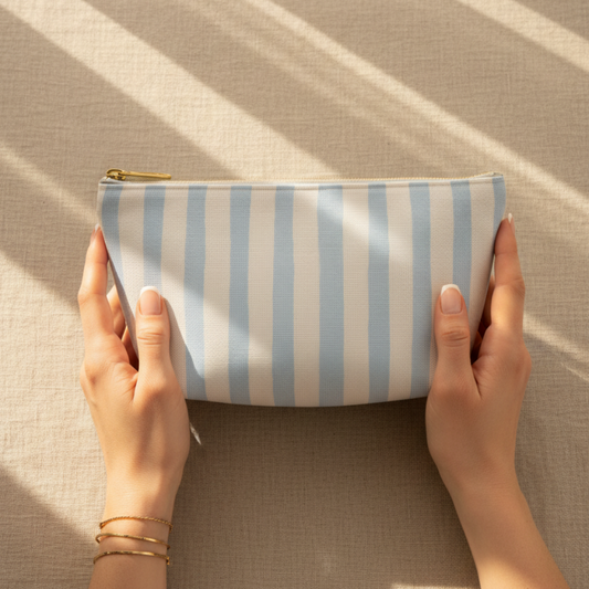 Hands holding a striped pouch on a textured surface with sunlight casting shadows.