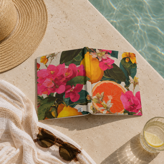 Floral notebook, sunglasses, and glass of lemonade on a sunlit poolside surface.
