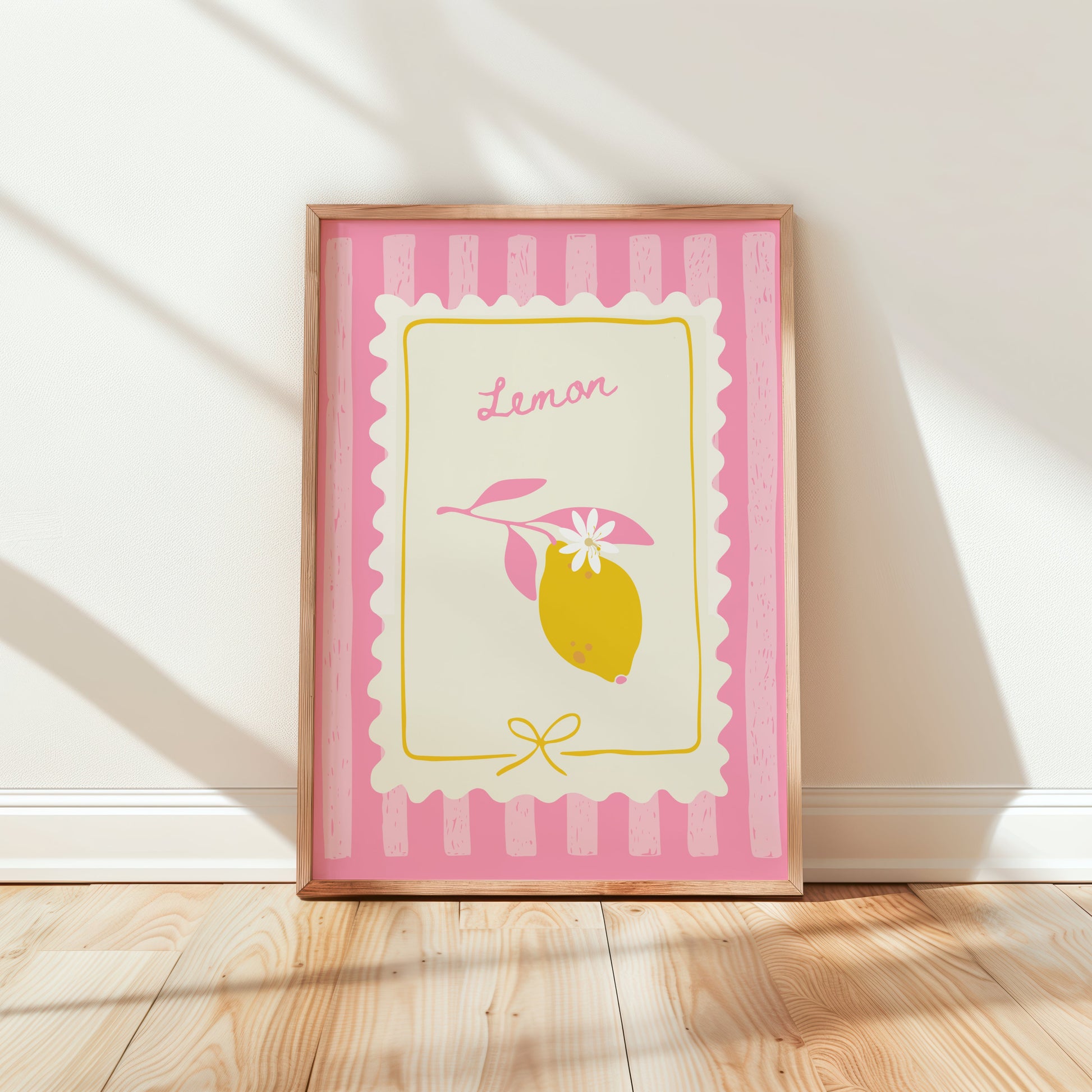 Framed artwork with a lemon design on a pink and white striped background, leaning against a white wall.