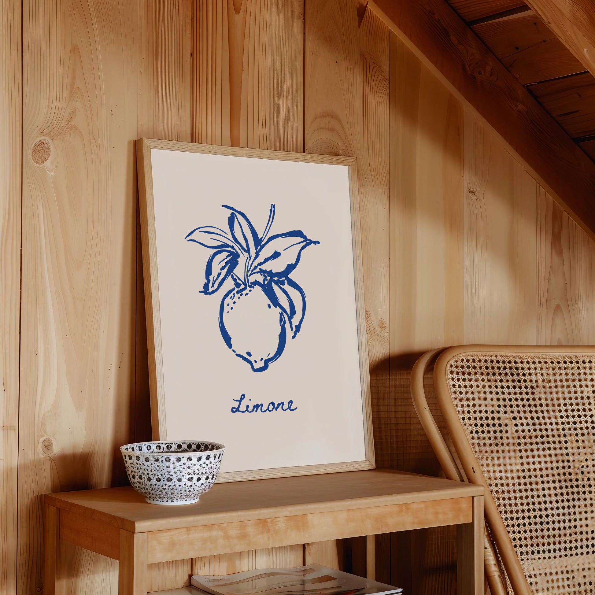 Framed artwork with blue lemon design on a wooden surface next to a wicker chair.