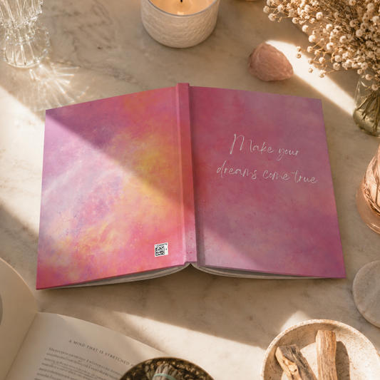 Open book with colorful cover and motivational quote "Make your dreams come true" on a table with decorative items.