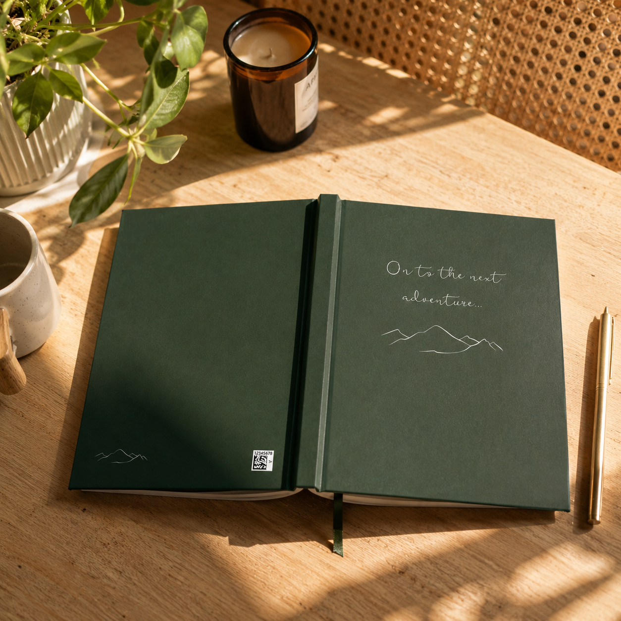 Open green notebook with 'On to the next adventure' text on a wooden table with a candle and plant.