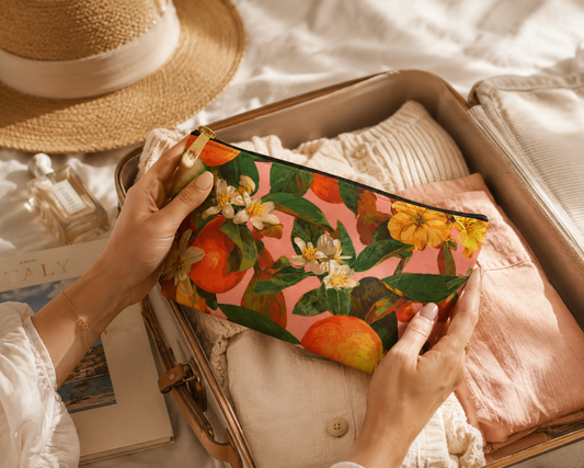 Person holding a floral orange blossom clutch with a suitcase and hat in the background