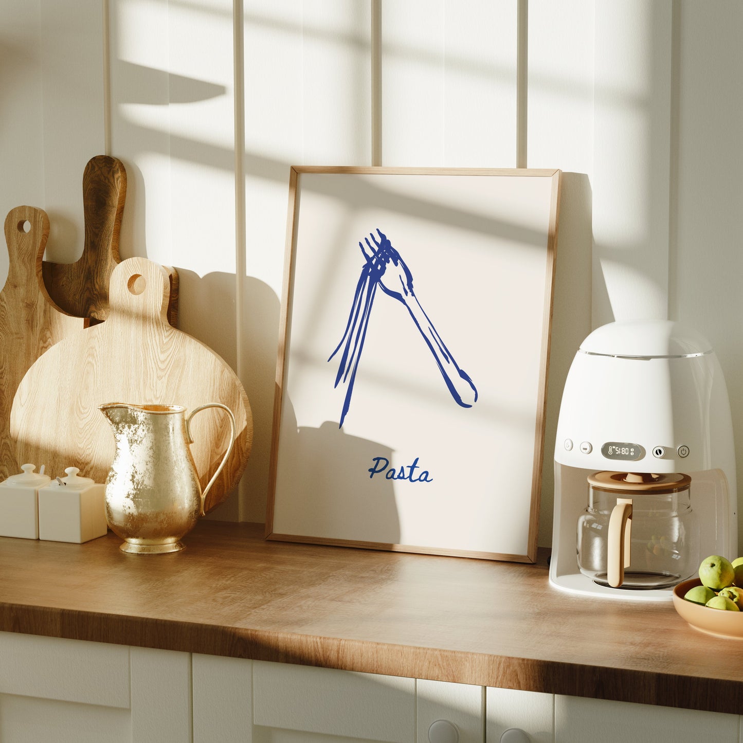 Kitchen counter with a coffee machine, bowl of fruit, and framed pasta artwork on a wooden surface.