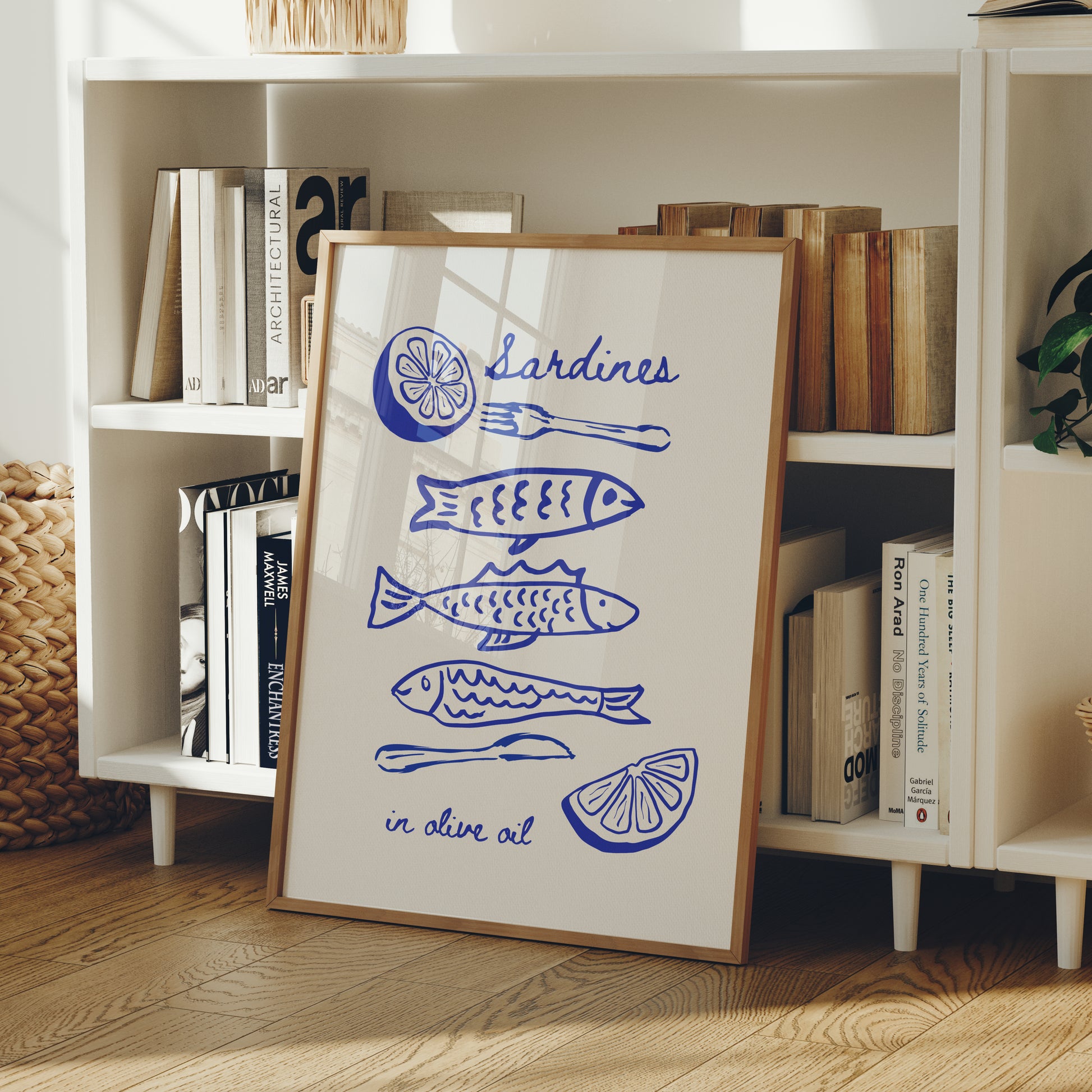 Framed artwork with blue fish illustrations on a white background, leaning against a bookshelf.