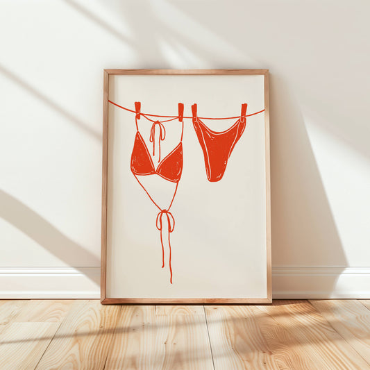 Framed artwork of a red bikini on a clothesline against a white wall.