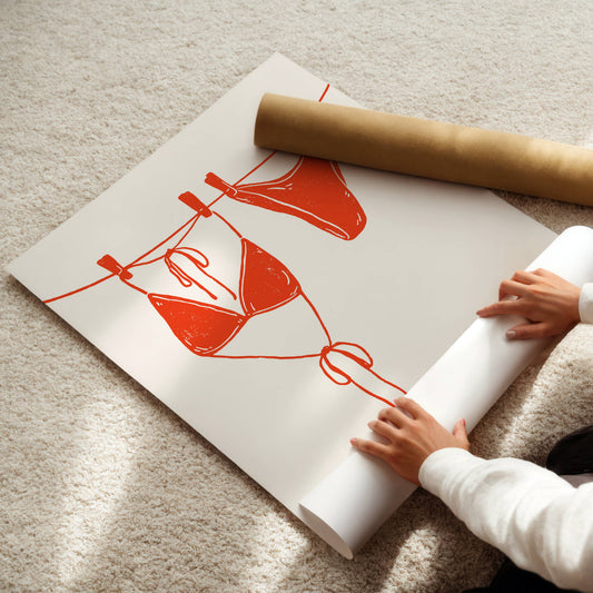 Person unrolling a large poster with red bikini graphics on a beige carpet