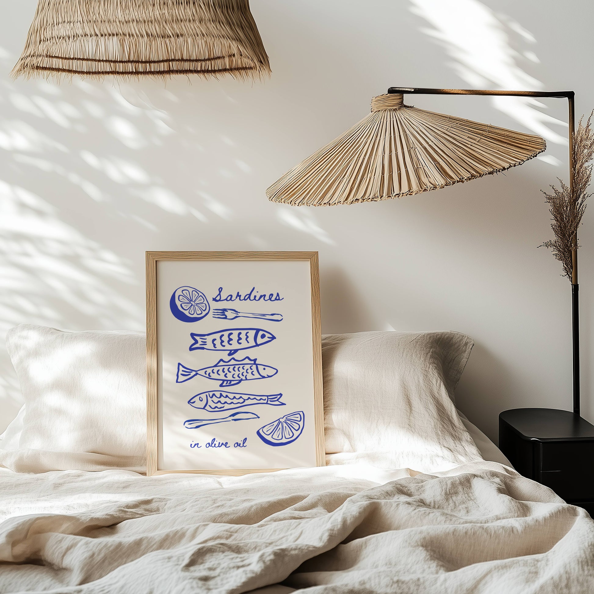 Framed artwork with blue illustrations on a bed with wicker lamps and white bedding.