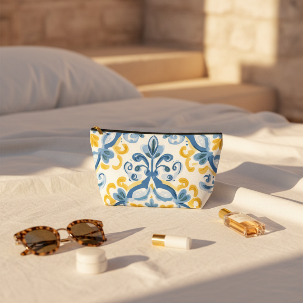 Blue and white patterned pouch on a bed with sunglasses, lip balm, and perfume bottle.
