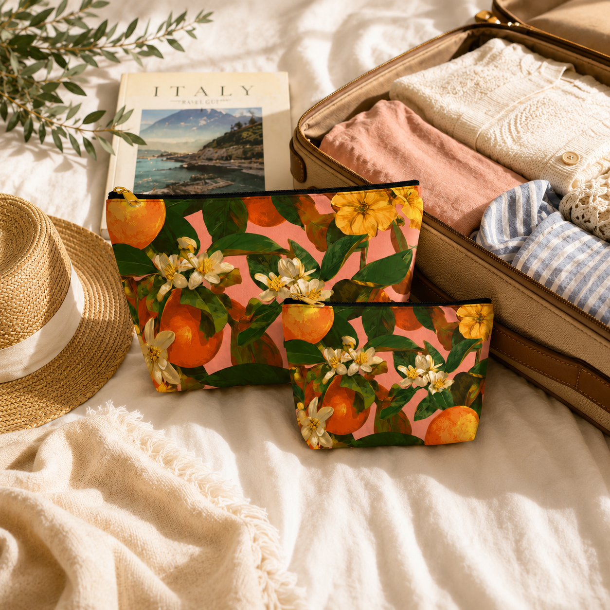 Floral pouches with oranges and flowers next to an open suitcase with clothes and a hat on a white surface.
