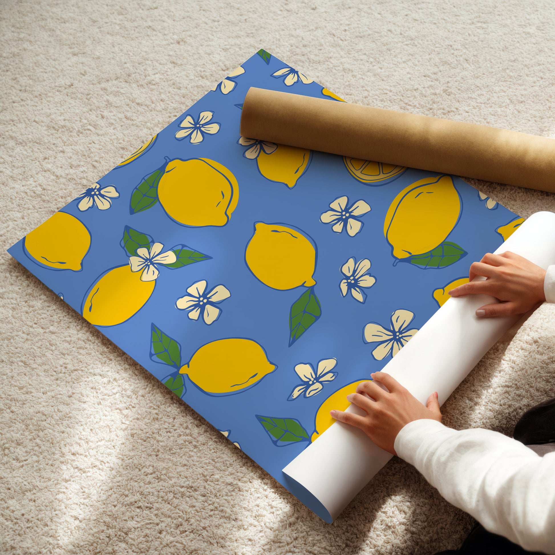 Person unrolling a roll of blue paper with lemon pattern on a beige carpet