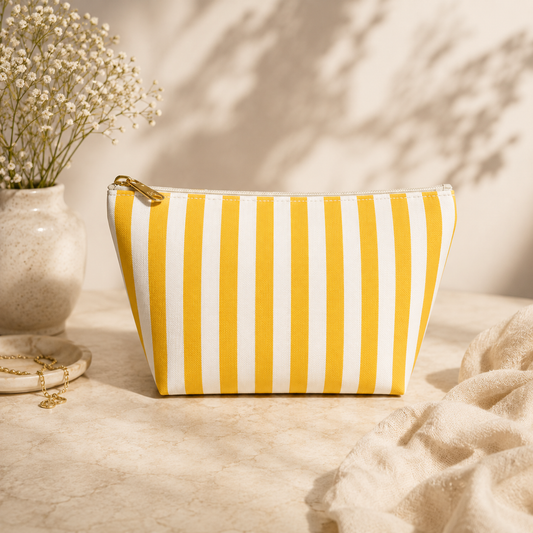 Yellow and white striped pouch on a textured surface with a vase of flowers in the background